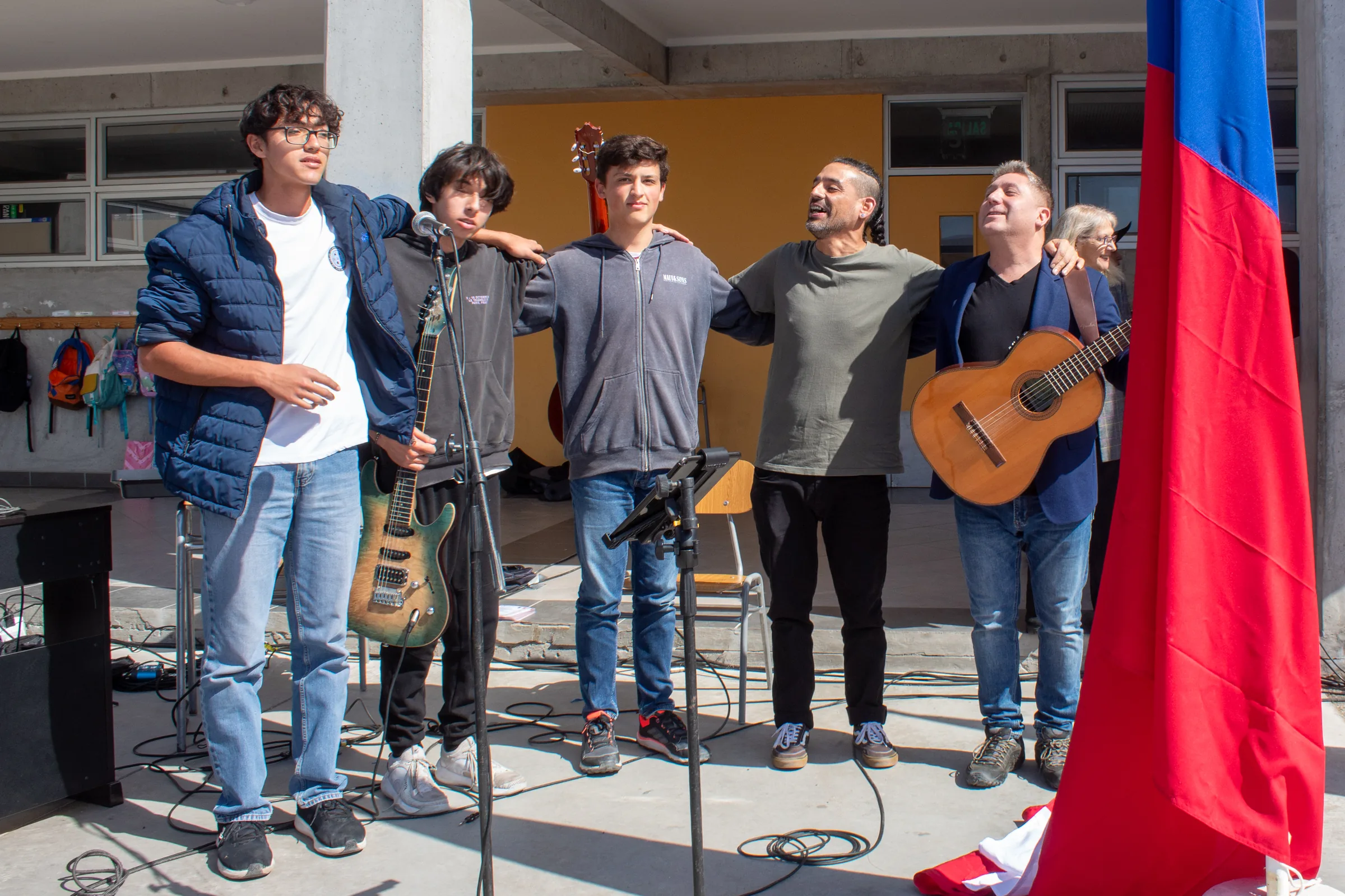 Grupo de músicos haciendo reverencia con bandera chilena al fondo
